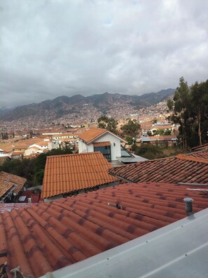 A residential area with terracotta-tiled roofs, a white building with a flat roof, and a mountainous backdrop. - New Day Cusco  (Cusco)