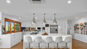 Een moderne keuken met witte kasten, roestvrijstalen apparatuur en een centraal kookeiland met barkrukken.