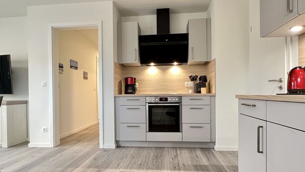 A modern kitchen with grey cabinets, a built-in oven, and a coffee maker.
