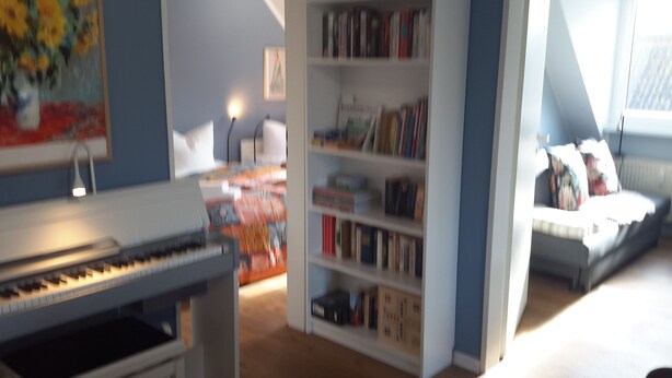 Una habitación con un piano, una estantería y una ventana.