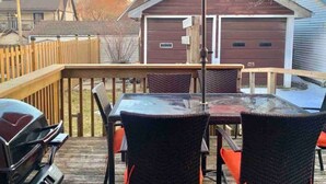 Une terrasse extérieure couverte, avec une table en verre et des chaises en osier, un barbecue et un parasol rouge.