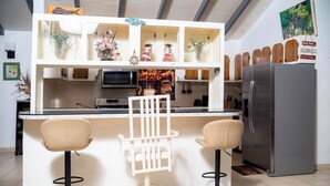 A kitchen with a central island, two bar stools, a refrigerator, and decorative items on the shelves.