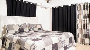 A bedroom with a large bed, black curtains, and a patterned quilt.