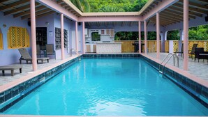 A swimming pool with a covered area, lounge chairs, and a small bar area.