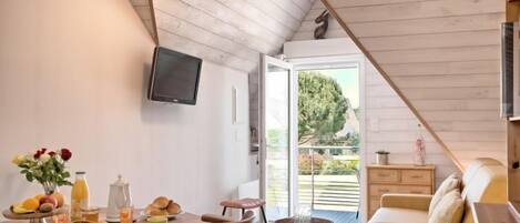 A cozy dining area with wooden furniture, a table set with breakfast items, and a TV mounted on the wall.