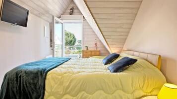 Een slaapkamer met een bed, een aan de muur bevestigde televisie en uitzicht op het buitenleven door een schuifdeur.