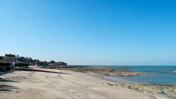 Une plage avec un ciel dégagé, un rivage sablonneux et des bâtiments en arrière-plan.