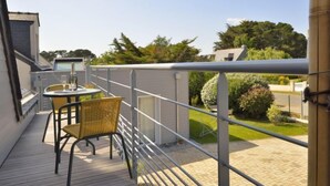 A balcony with a table and chairs, a metal railing, and a view of a garden and buildings.