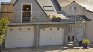A two-story house with a garage, a balcony with outdoor furniture, and a spiral staircase.