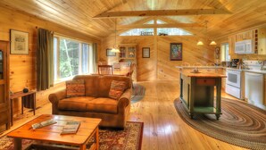 A cozy cabin interior with a wooden floor, a sofa, a dining table, and a kitchen area with a microwave and cabinets.