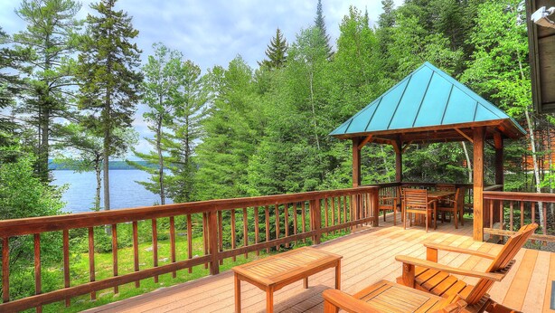 A wooden deck with outdoor furniture and a gazebo overlooking a lake.