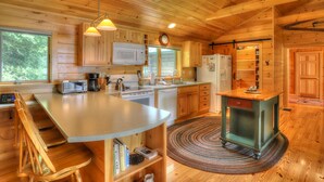 A wooden cabin kitchen with a central island, wooden cabinets, a microwave, a sink, and a refrigerator.