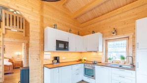 A modern kitchen with white cabinets, a microwave, an oven, and a sink. There is a window with plants on the counter.
