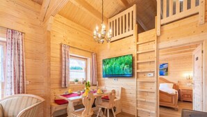 A cozy wooden cabin interior with a dining area, a bed, and a television mounted on the wall.