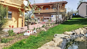 A wooden house with a balcony, a garden with a pond, and a clear sky.
