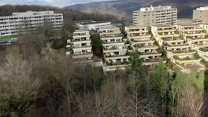 Zona residencial con varios edificios de apartamentos, rodeada de árboles y colinas al fondo.