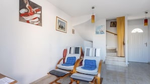 Uma sala de estar ampla com escada, cadeiras de madeira com almofadas azuis e piso de azulejos.