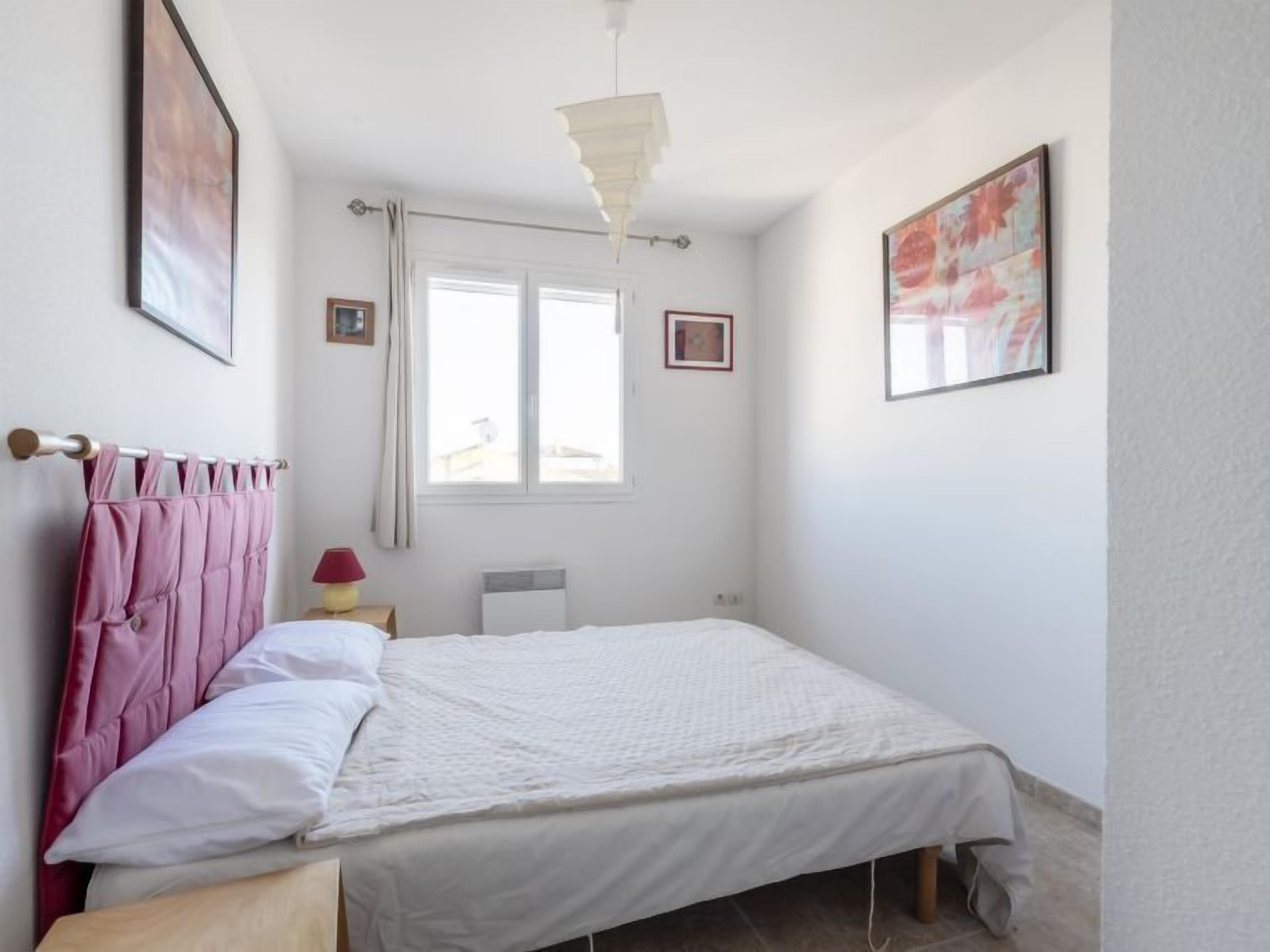 A bedroom with a bed, a window with curtains, a bedside lamp, and a ceiling light fixture.