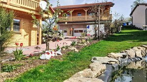 Une maison en bois avec un balcon, un jardin avec un étang et un ciel dégagé.