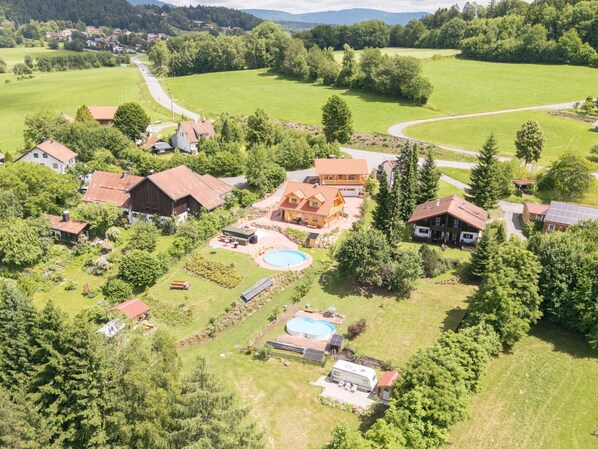 An aerial view of a rural property with multiple buildings, a swimming pool, and surrounding greenery.