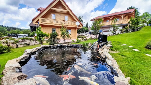 Une maison en bois avec un étang et des carpes koï.