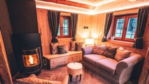 L’intérieur d’un chalet confortable, avec une cheminée, des murs en bois, un canapé et un fauteuil rembourré.