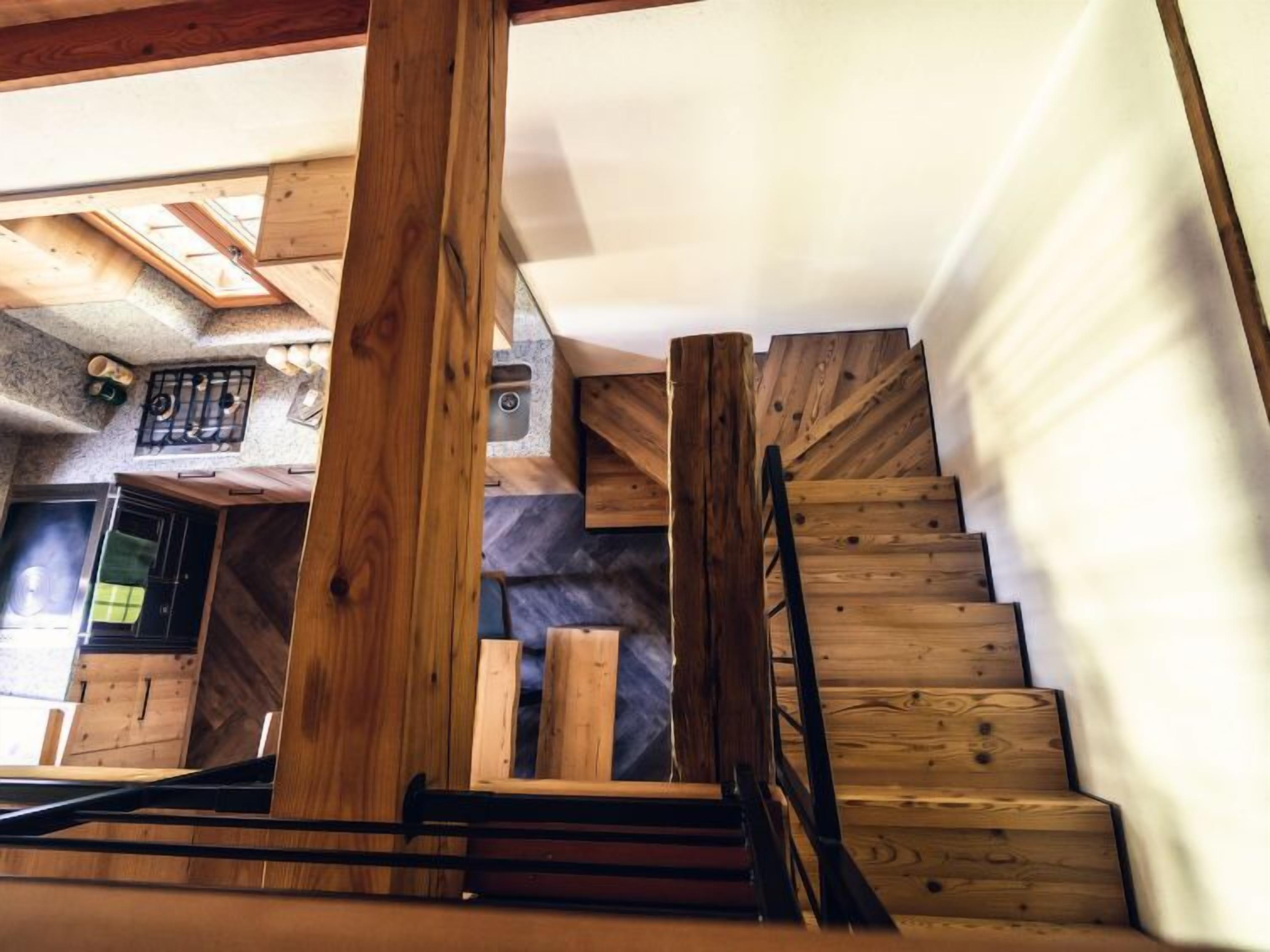 Un escalier en bois avec une rampe, menant à une pièce comprenant un coin cuisine et une fenêtre.