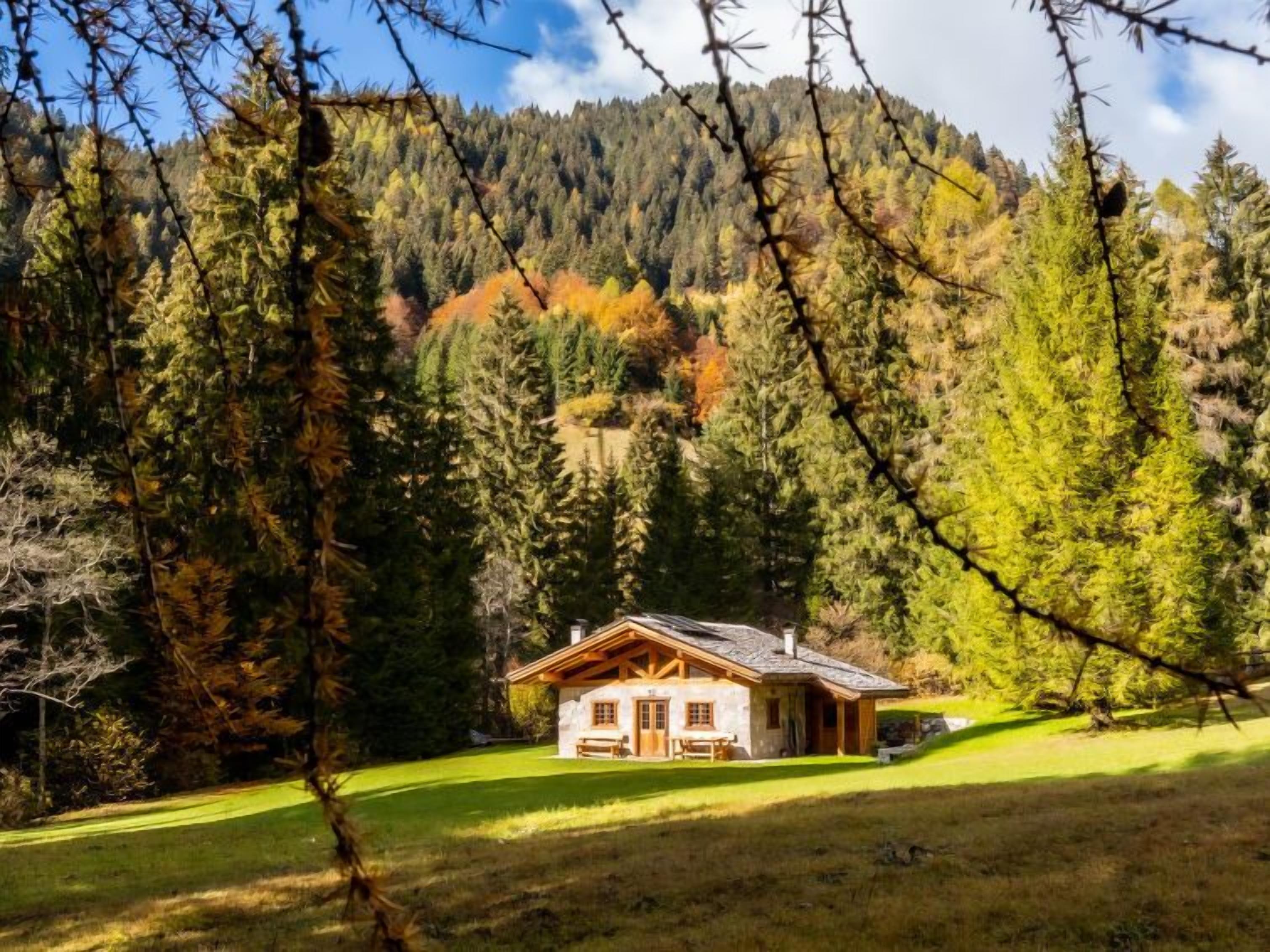 Eine rustikale Holzhütte mit Natursteinaußenwand, einer Holzterrasse und Blick auf einen bewaldeten Berg.