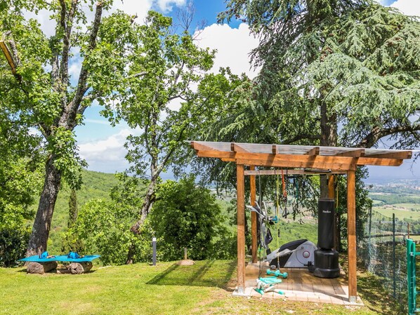 An outdoor gym area with exercise equipment, a covered seating area, and a scenic view of trees and hills.