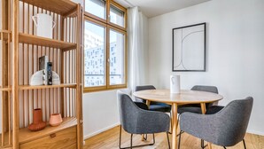 Une pièce moderne avec une table ronde en bois, des chaises grises à revêtement en tissu, une bibliothèque en bois et une fenêtre donnant sur des immeubles.