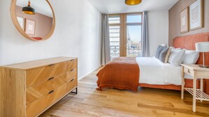 Une chambre moderne avec une commode en bois, un lit doté d’une tête de lit rouge, un miroir rond et une suspension.