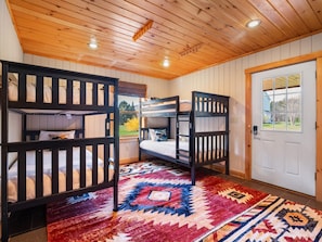 A room with bunk beds, a patterned rug, wooden walls, and a door with a window.
