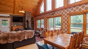 A cozy cabin interior with a stone fireplace, wooden dining table, and large windows. - The Lone Star- Hot Tub, AC, Pool Table (Newry)