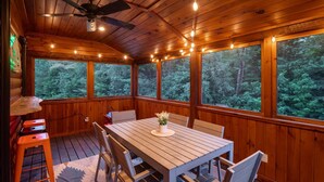 A wooden deck with a table and chairs, a ceiling fan, and large windows with a forest view. - The Lone Star- Hot Tub, AC, Pool Table (Newry)