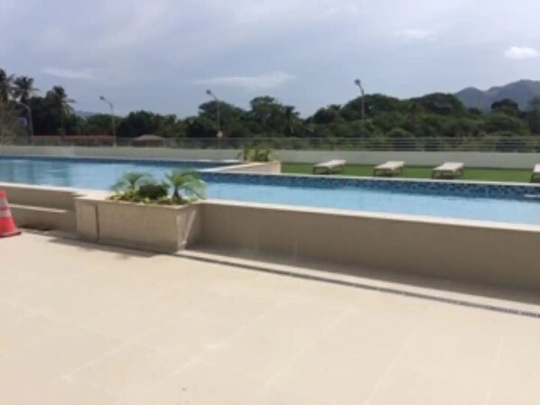 Une piscine avec une terrasse carrelée, quelques chaises longues et un petit jardin agrémenté de plantes.