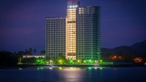 Ein Hochhaus-Hotel mit mehreren Etagen, einem gut beleuchteten Hauptturm und Blick auf das Wasser.