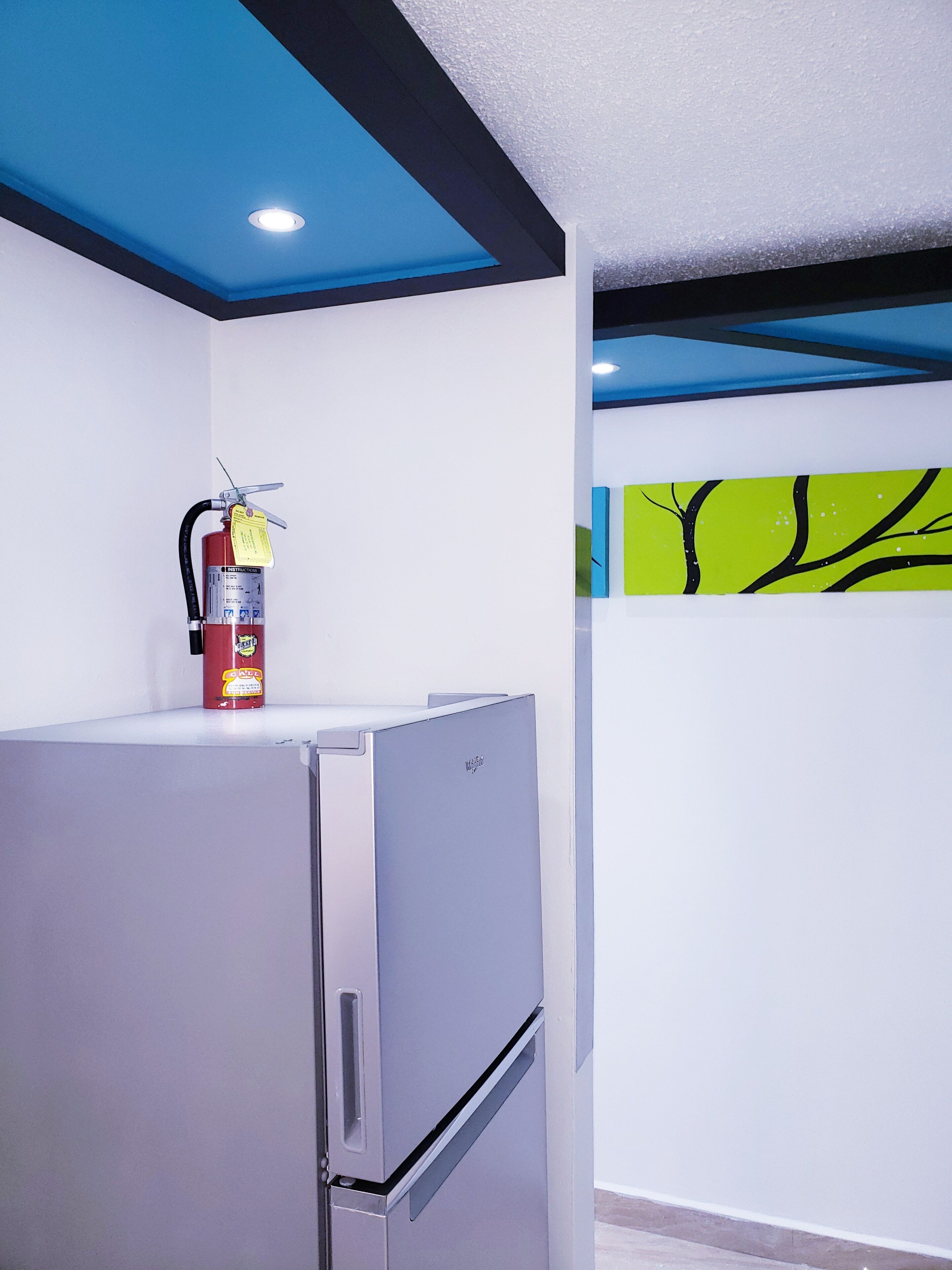 Una cocina moderna con un refrigerador de acero inoxidable, un extintor en la encimera y una pared con diseño de rama de árbol.