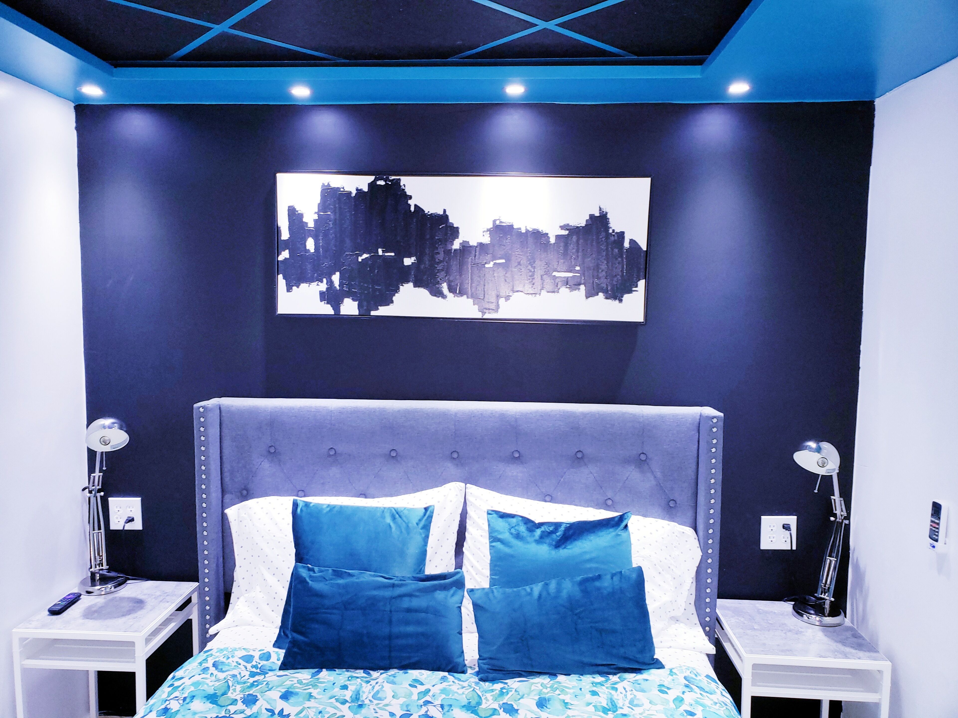 Un dormitorio moderno con cabecera capitonada, una obra de arte urbana y una colcha con estampado floral.