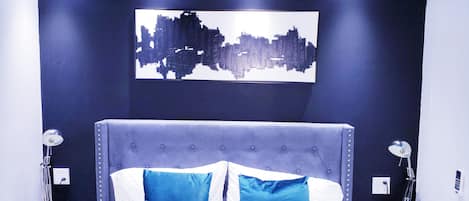 Un dormitorio moderno con cabecera capitonada, una obra de arte urbana y una colcha con estampado floral.