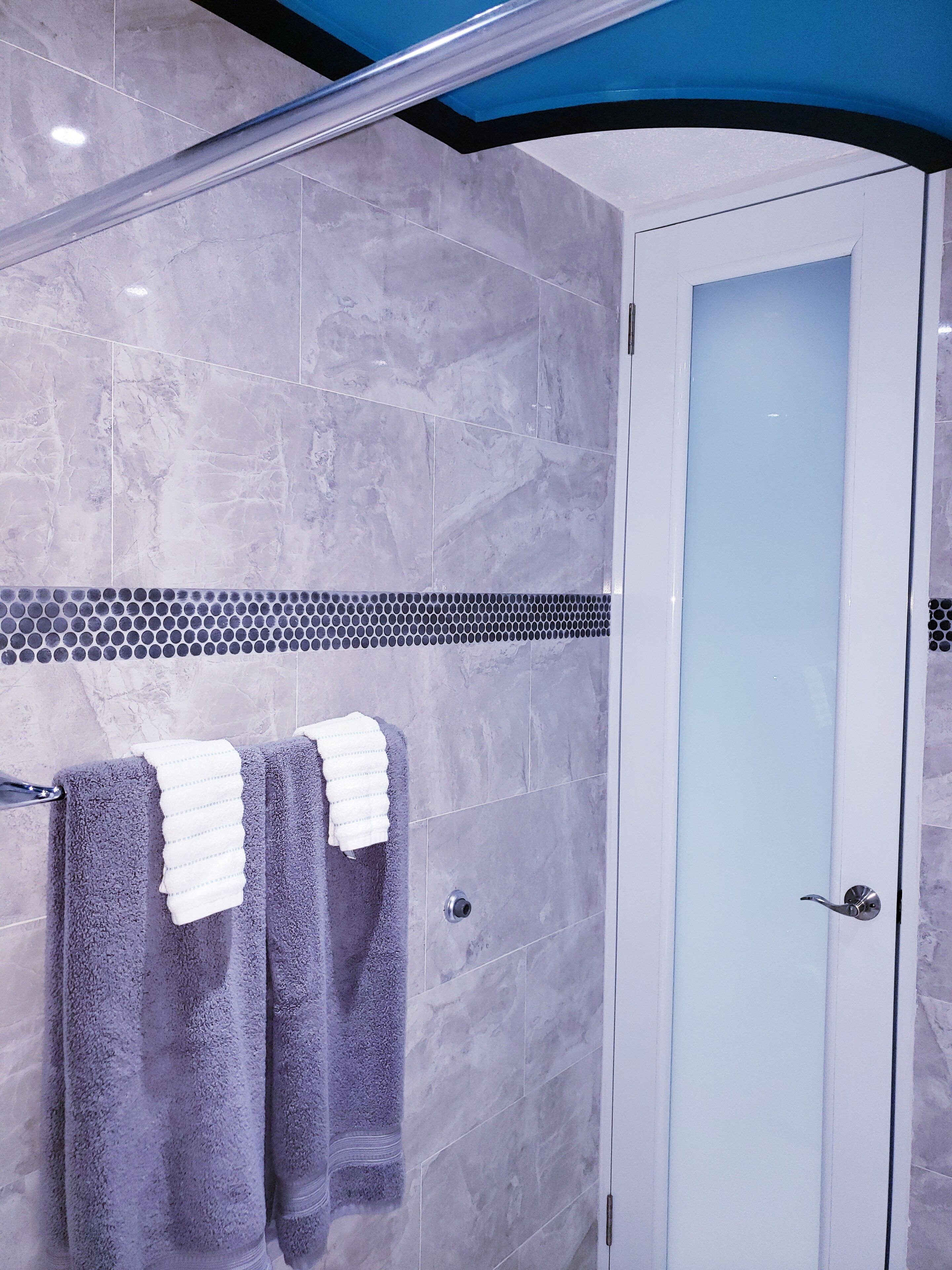 Ein modernes Badezimmer mit grauen Marmorfliesen, einer Glasdusche und einer weißen Tür.