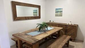 Une table à manger en bois, accompagnée de bancs, un miroir et un meuble, dans une pièce dont le sol est recouvert de carreaux.