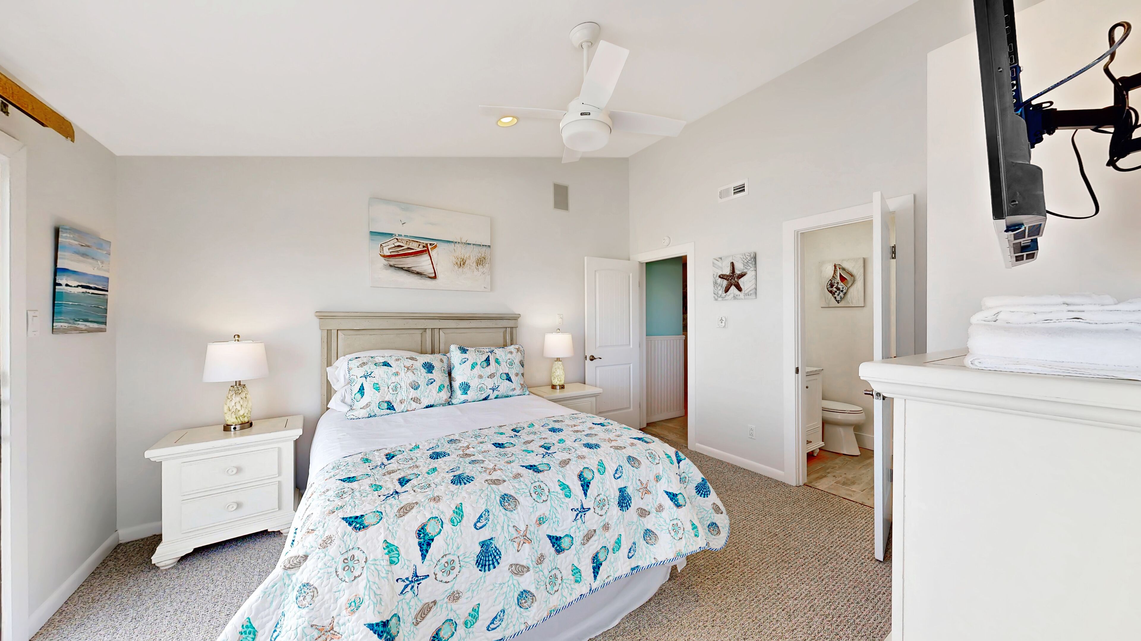 A bedroom with a bed, nightstands, a ceiling fan, a bathroom with a toilet and sink, and a towel rack.