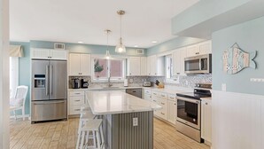 A modern kitchen with a central island, stainless steel appliances, and a decorative wall piece. - 6 Bedroom Oceanfront House in N. Bethany Beach. Renovated in 2024. Watch video! (Bethany Beach)