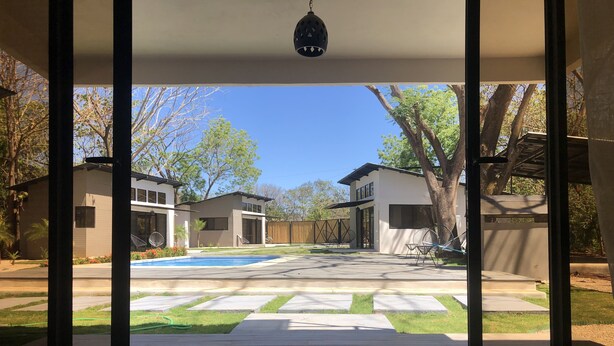 Een uitzicht op een achtertuin met een zwembad, twee moderne huizen en een pergola.
