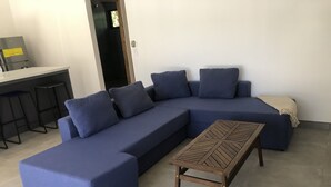 Een moderne woonkamer met een hoekbank, een houten salontafel en een bar met barkrukken.