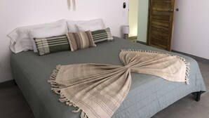 Een bed met een groene sprei, meerdere kussens, een macramé wanddecoratie en een houten deur.