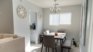 A modern living room with a sofa, dining table, chairs, and a chandelier.