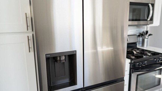 A stainless steel refrigerator with a water dispenser, a microwave, and a stove in a kitchen.