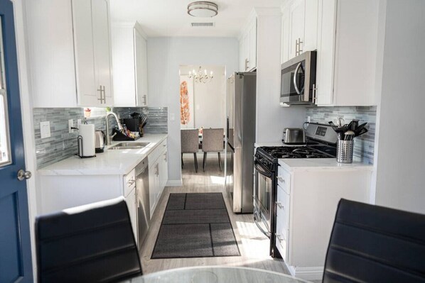 A modern kitchen with white cabinets, a stove, microwave, and a dining area with a table and chairs.