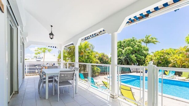 Un espace extérieur abrité comprenant une piscine, une table avec des chaises et une vue sur la verdure environnante.